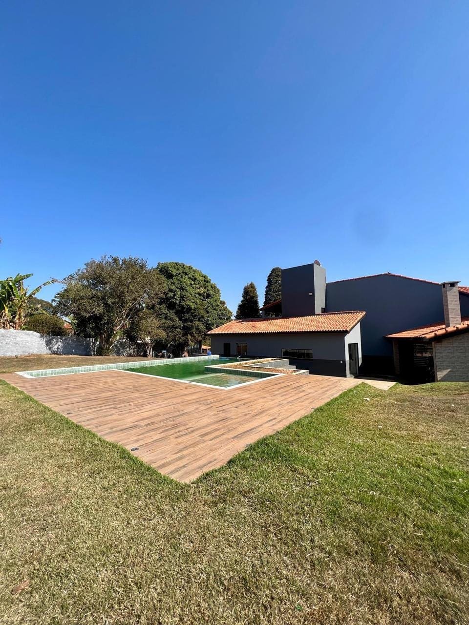 Piscina com deck de madeira e a sede ao fundo